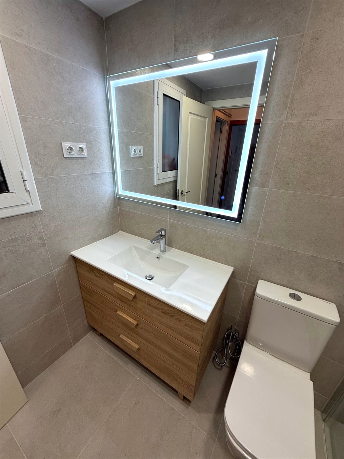 Mueble de baño con lavabo sobre encimera y espejo retroiluminado