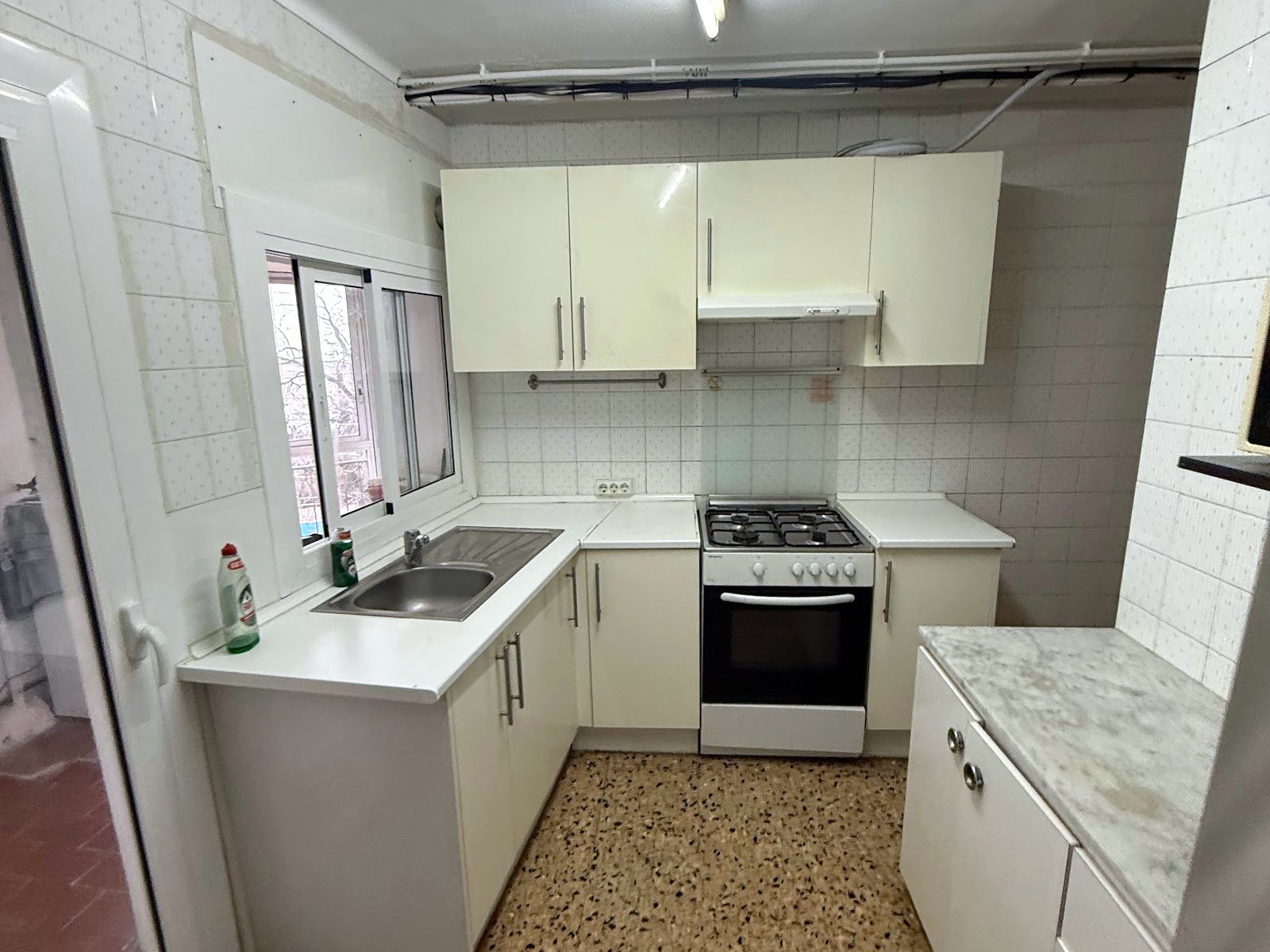 Cocina antes de la reforma vista desde la puerta, con muebles antiguos y suelo de terrazo